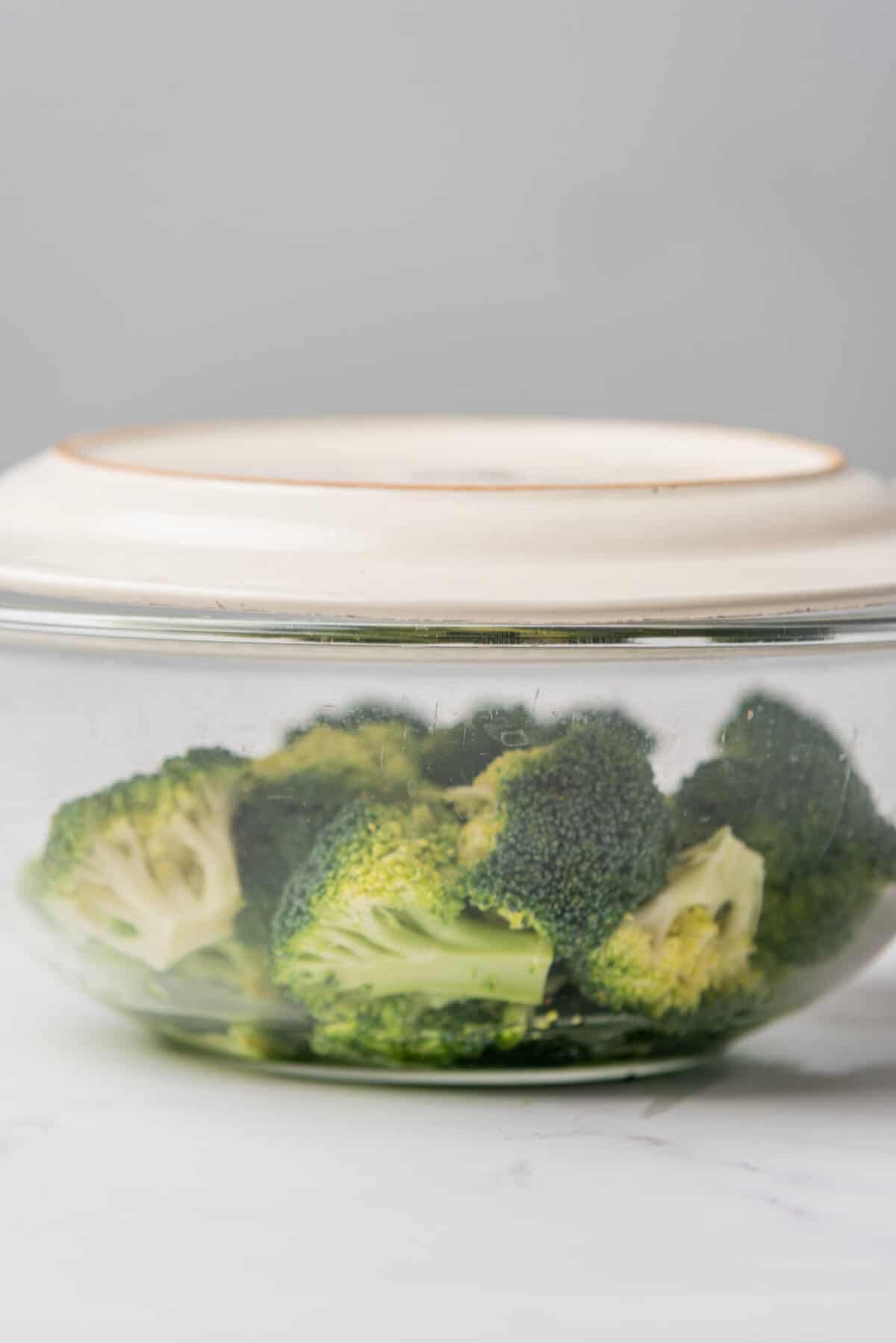 An image of broccoli in a bowl being covered by a plate