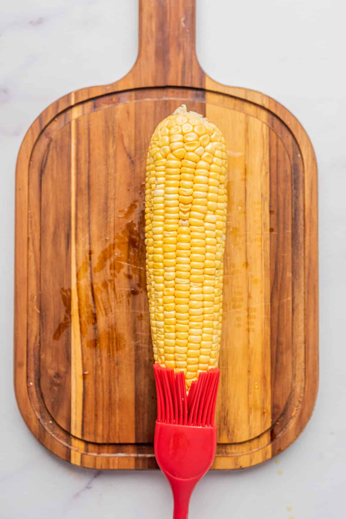 An image of a corn being brushed with butter on a chopping board