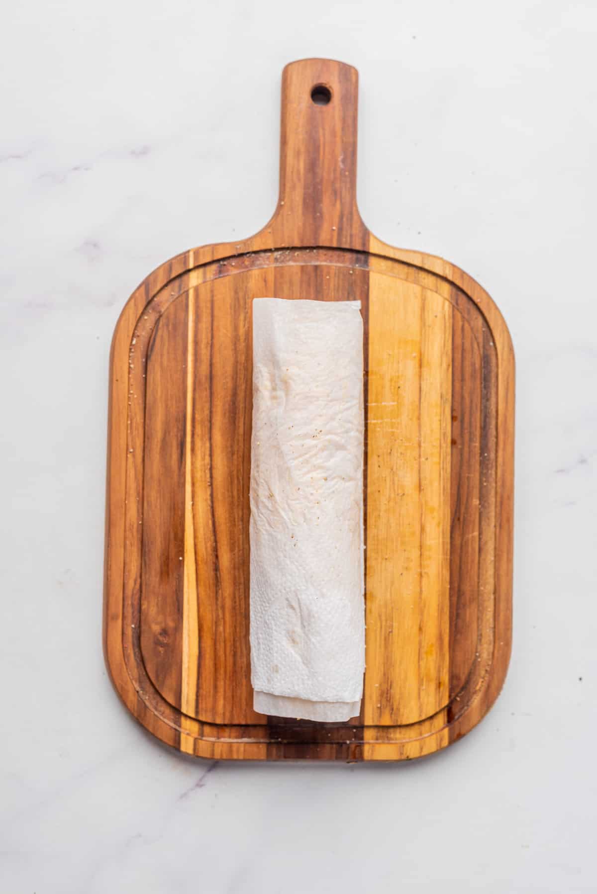 An image of a corn wrapped in a paper towel on a chopping board