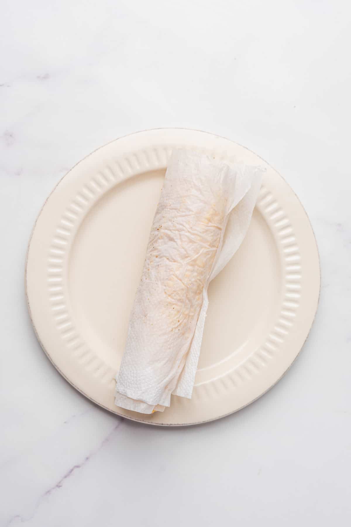 An image of a corn covered with a damp paper towel on a microwave-safe dish