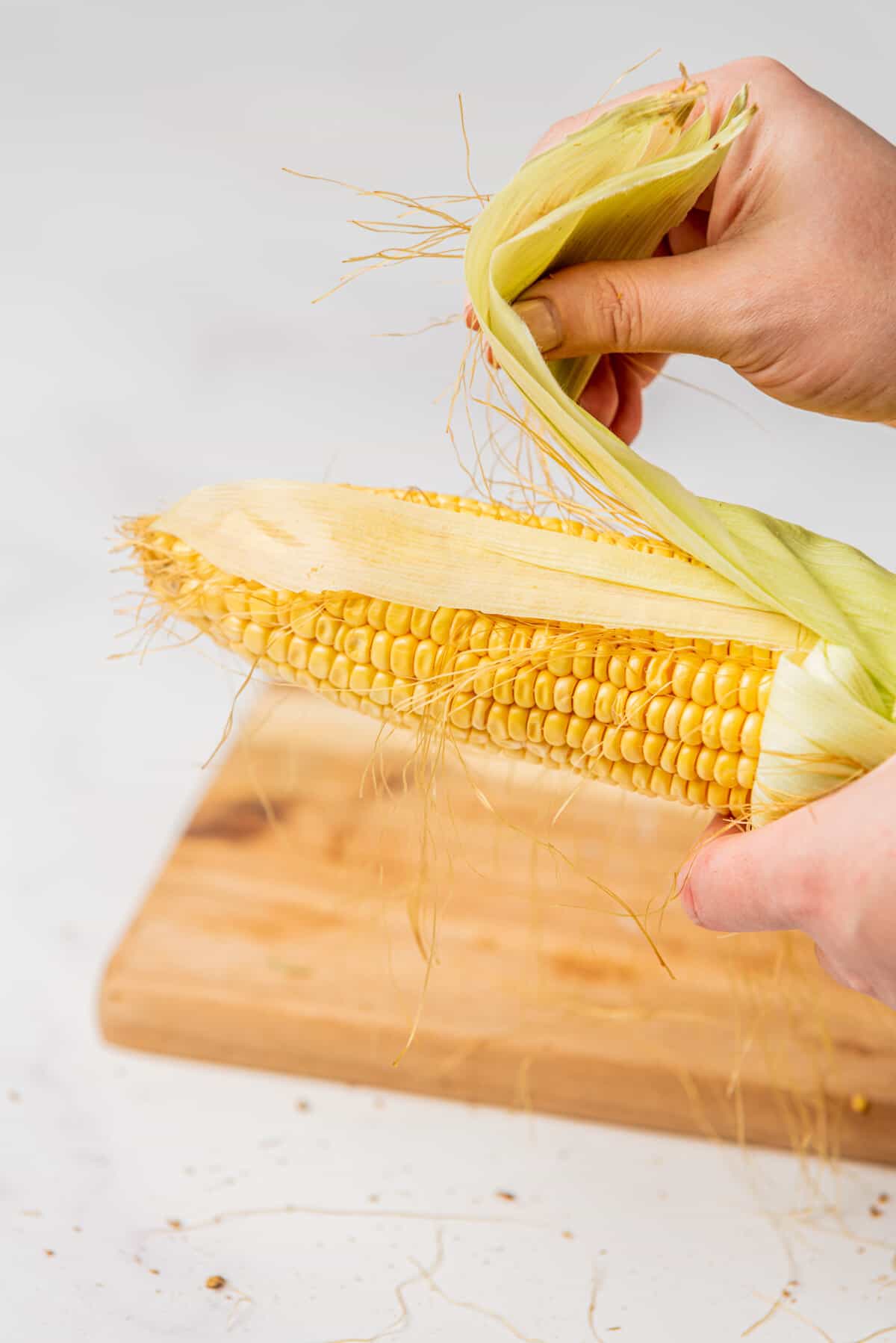 An image of the process of removing corn husk and silk on a sweet corn