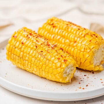 An image of a halved corn on a plate topped with chili flakes