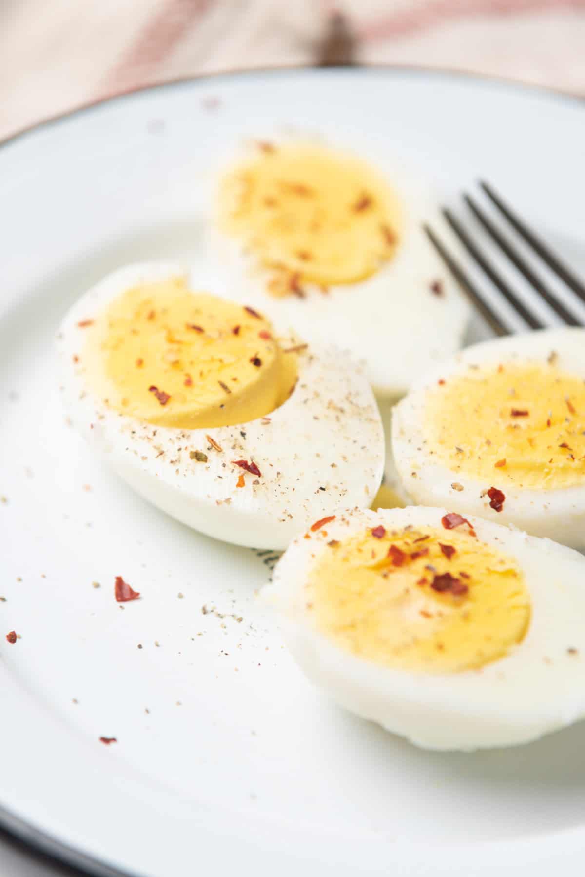 An image of two hard boiled eggs sliced in half, topped with seasonings, and being served on a plate with a fork behind them.