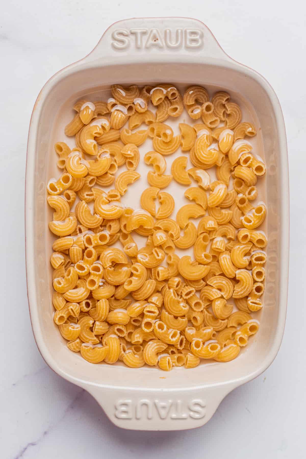 An overhead image of uncooked elbow macaroni pieces in a baking dish.