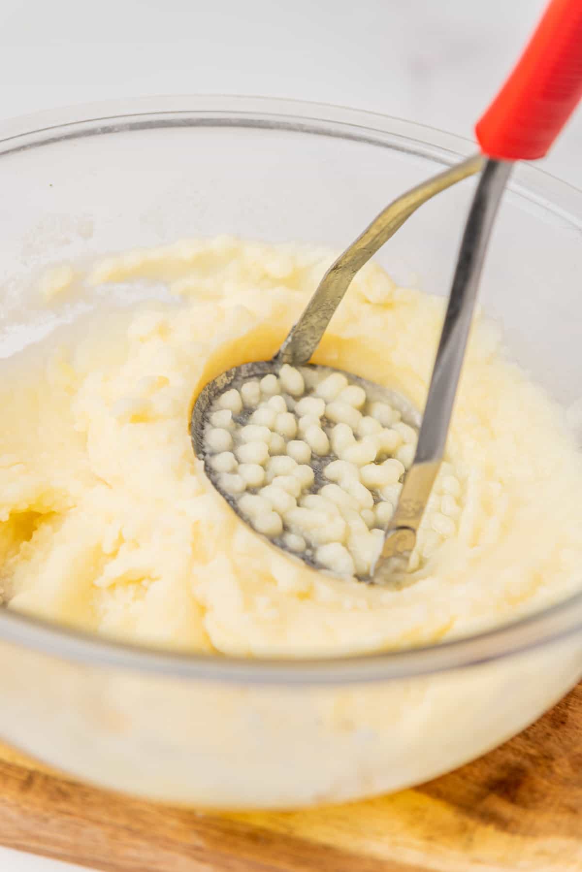A closeup image of potatoes being mashed by a potato masher in a bowl..