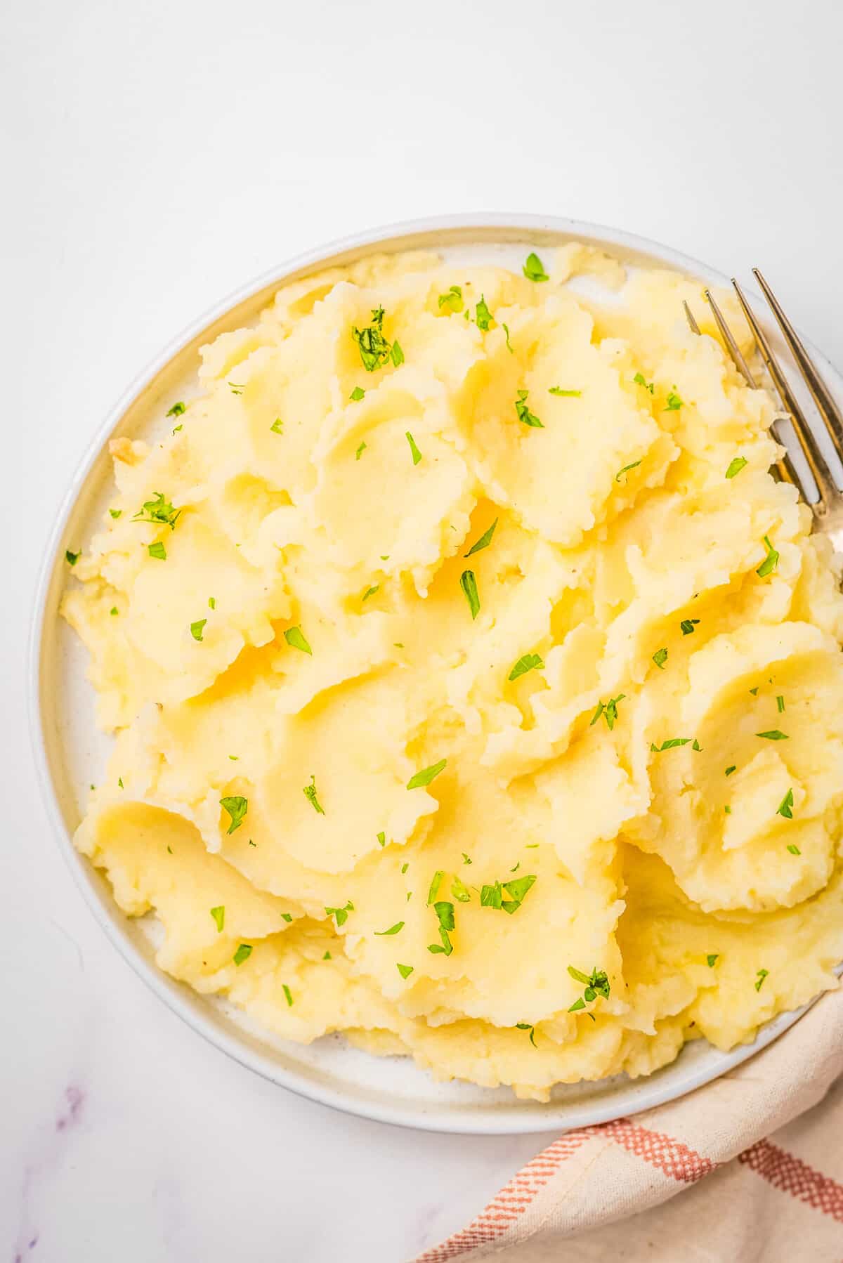 An overhead image of microwave mashed potatoes in a bowl with fresh herbs on top and a fork resting on the right side of the bowl.