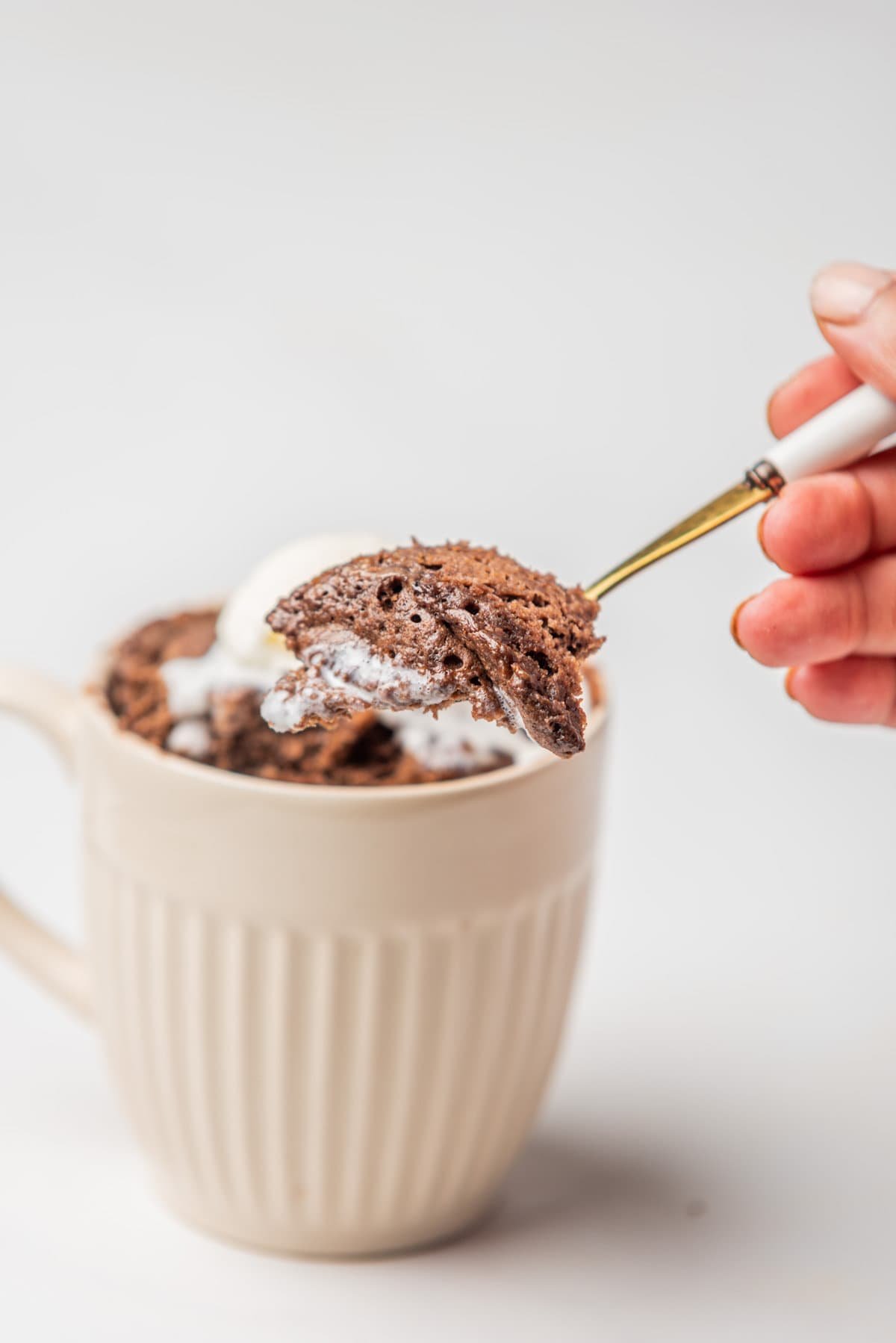 An image of a hand scooping out a spoonful of chocolate mug cake.