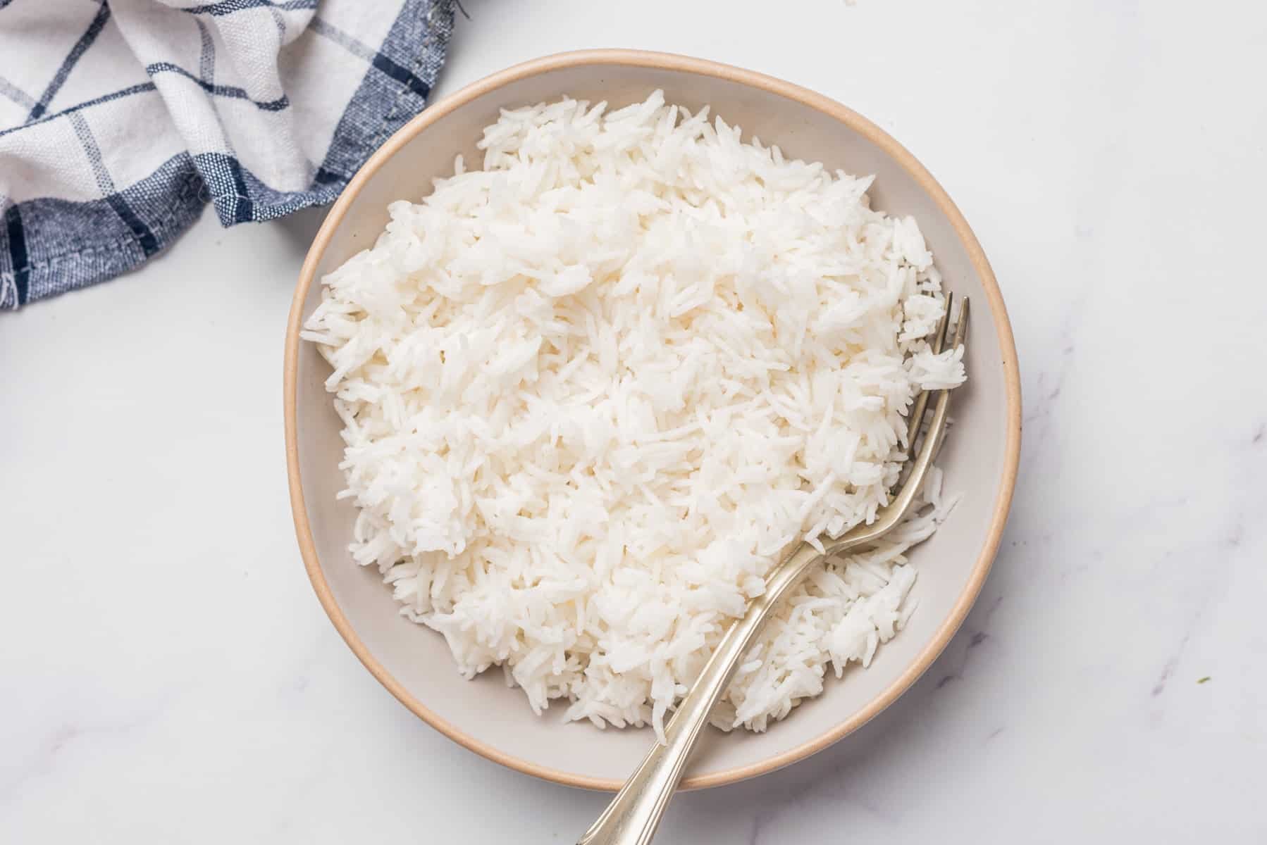 An image of a bowl full of white basmati rice with a spoon sitting on top of the rice.