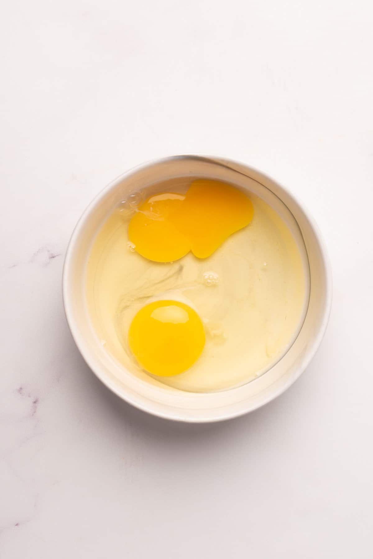 An overhead image of two uncooked eggs in a ramekin.