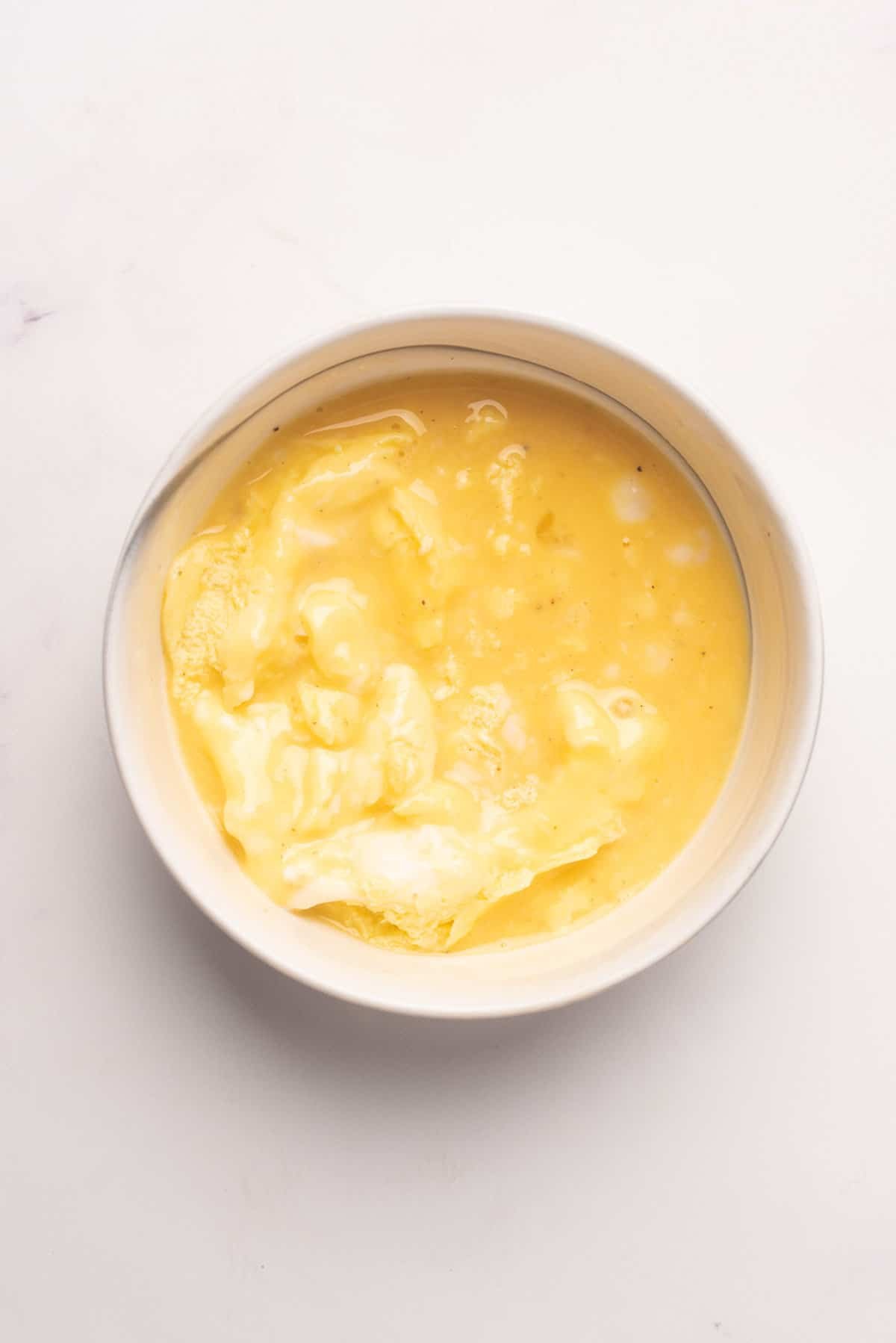 An overhead image of eggs mixture in a ramekin after microwaving for 1 and a half minutes.