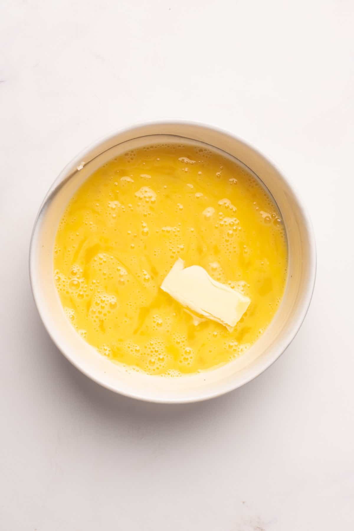 An image of butter being added to the scrambled eggs mixture.