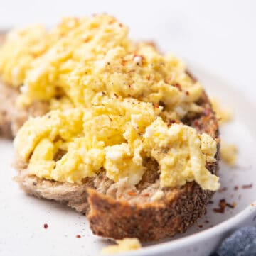 A closeup image of microwave scrambled eggs on a toast served on a plate.