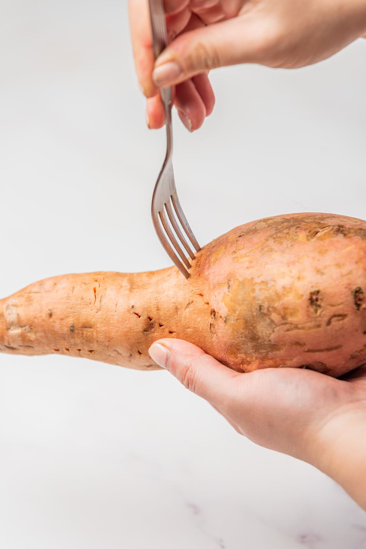 An image of a hand holding a sweet potato while being pierced by a fork.
