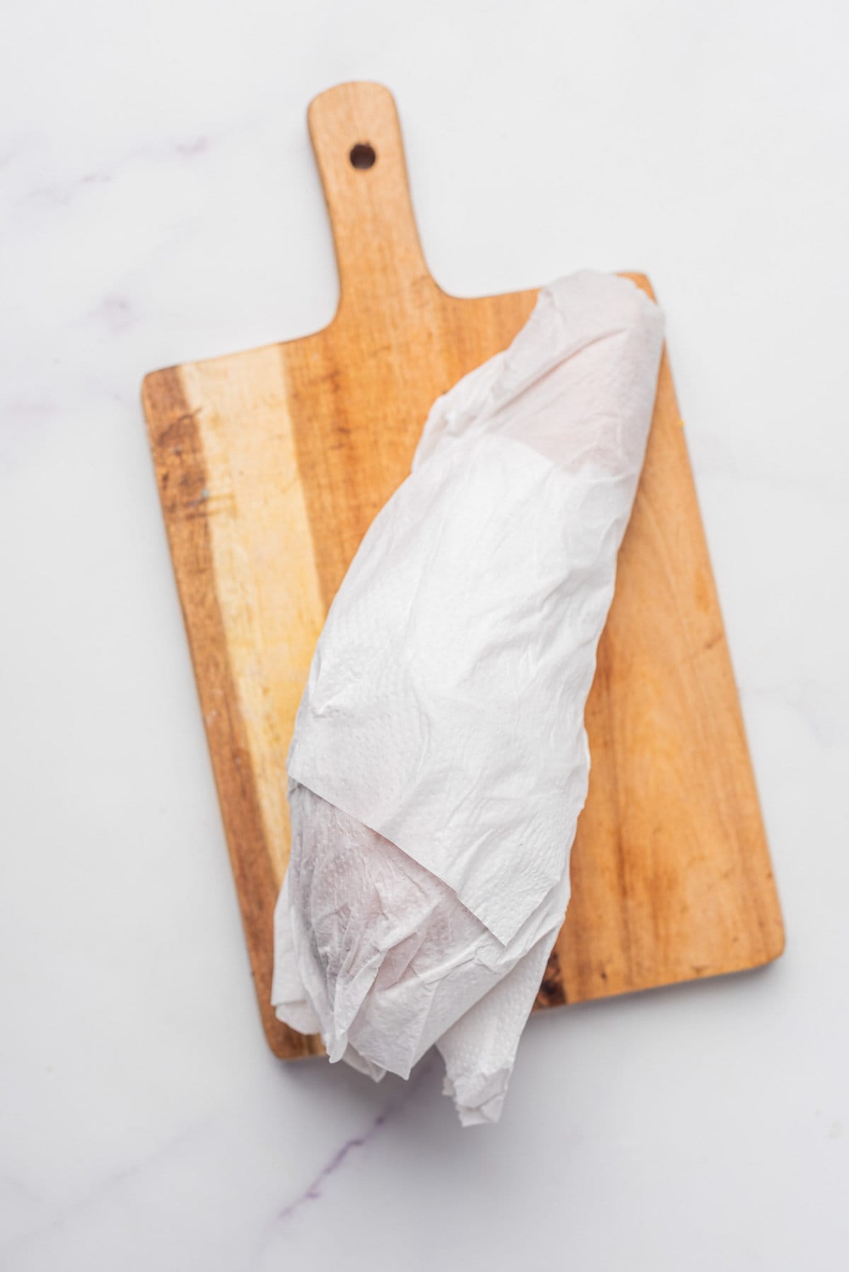 An image of sweet potato wrapped in a paper towel while resting on a chopping board.