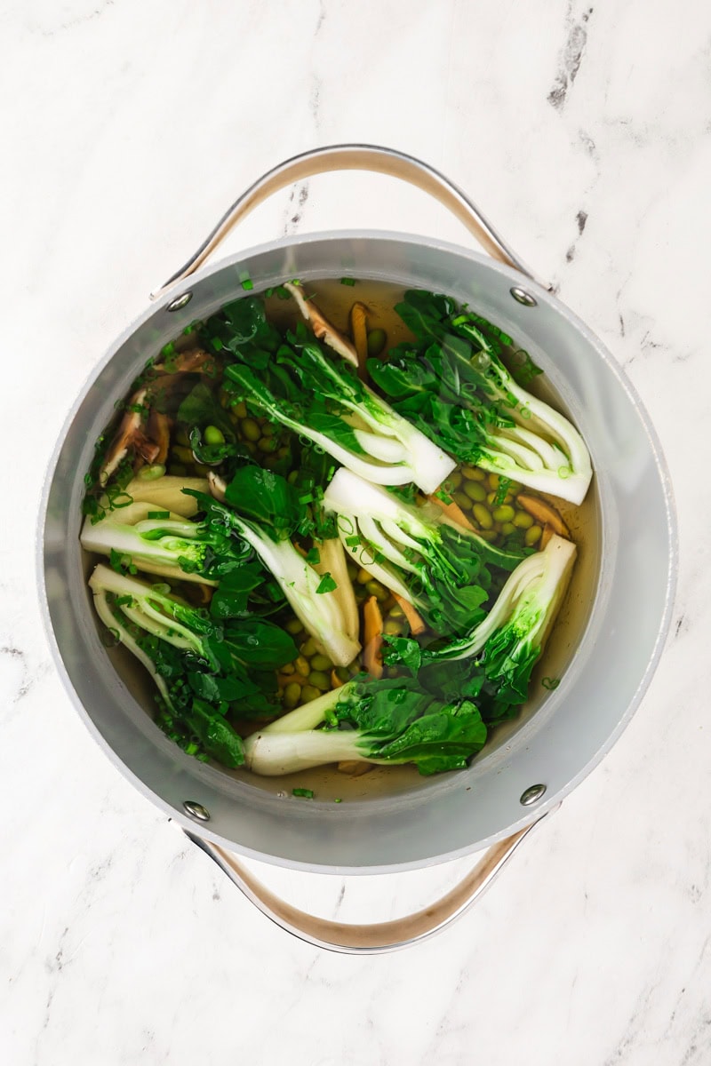 An overhead image of adding bok choy, edamame, and onions to the pot.