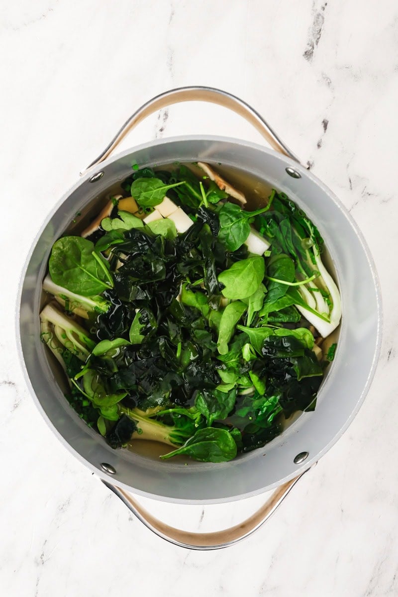An overhead image of adding spinach to the pot.