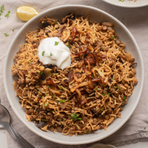 Bowl of mujaddara topped with crispy caramelized onions and a dollop of yogurt.
