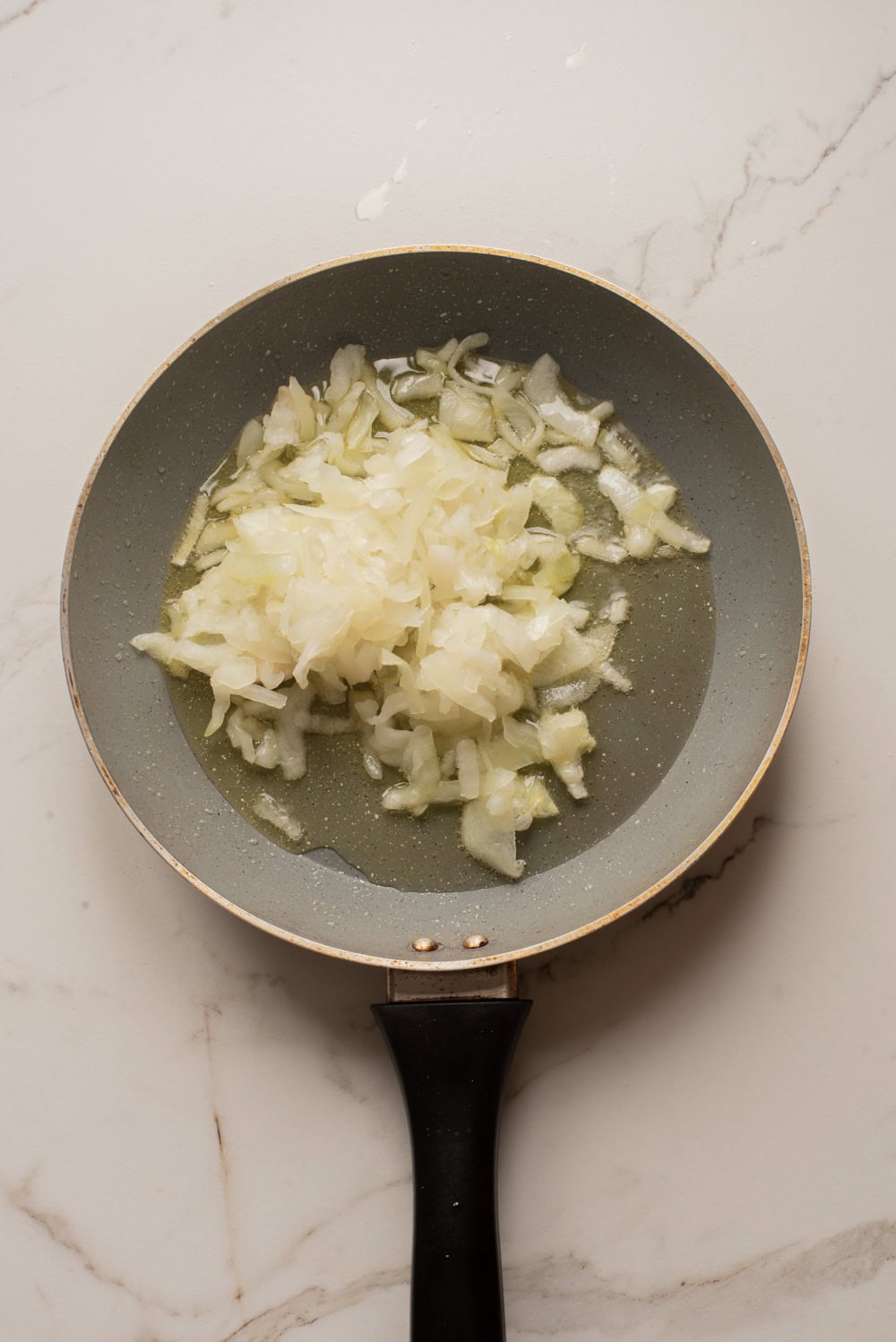 Sliced onions cooking in olive oil in a skillet.