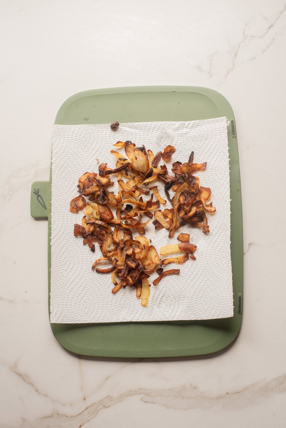 Crispy caramelized onions resting on a paper towel-lined plate.