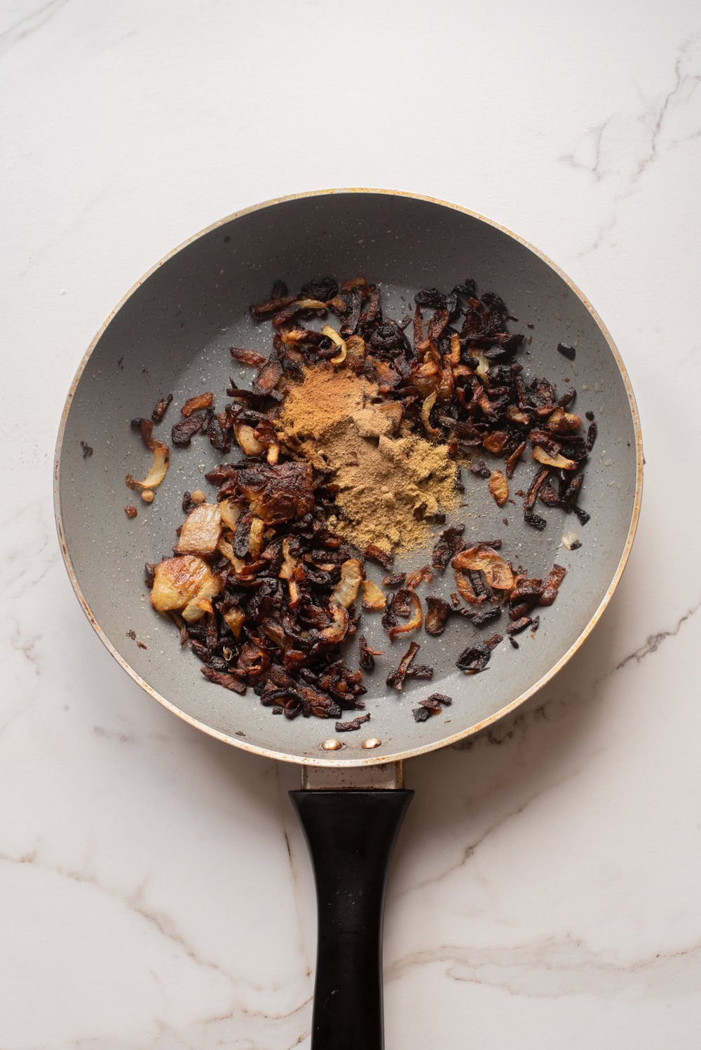 Caramelized onions in a skillet with spices added before mixing with rice and lentils.