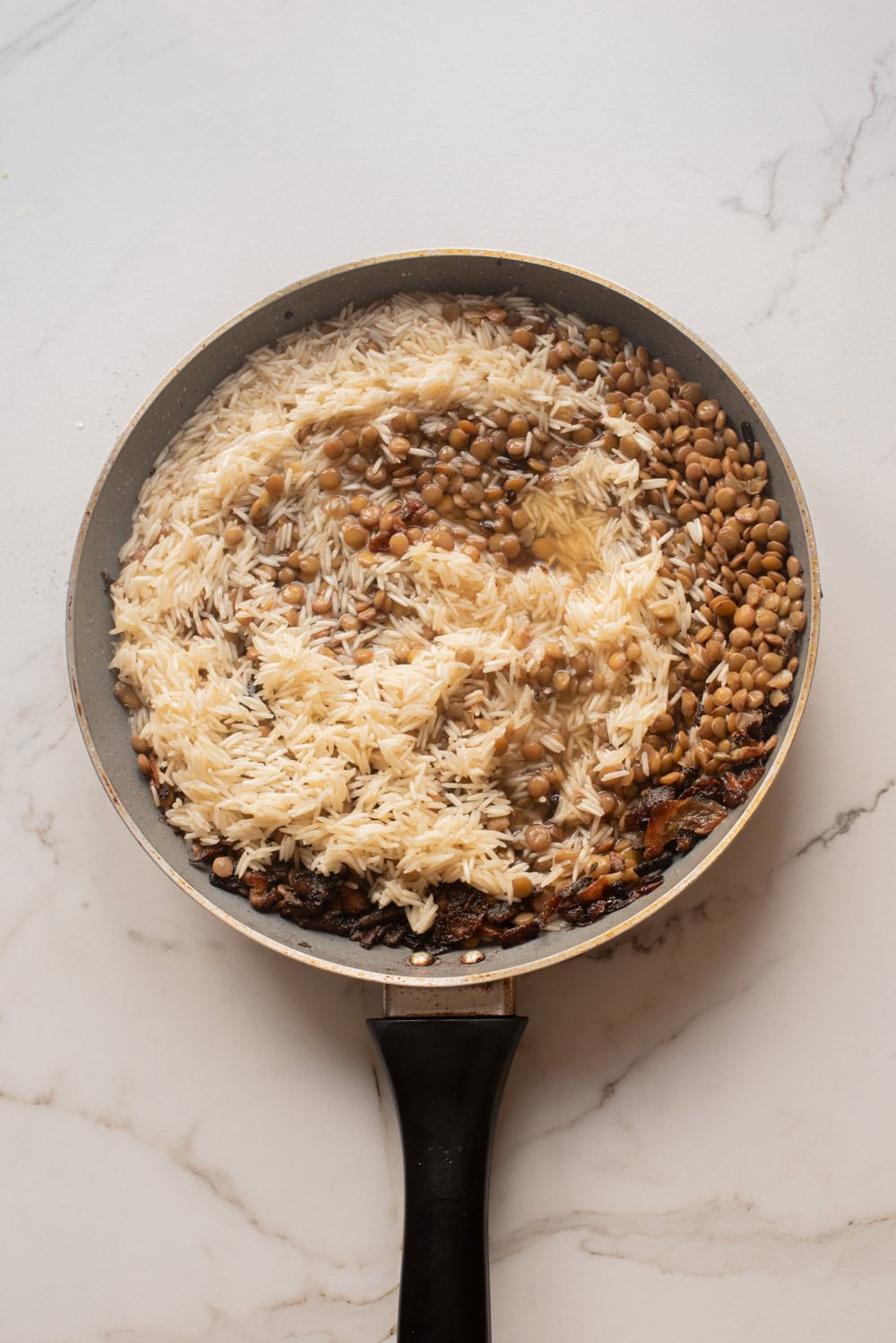 Rice and lentils combined in a skillet for mujaddara.