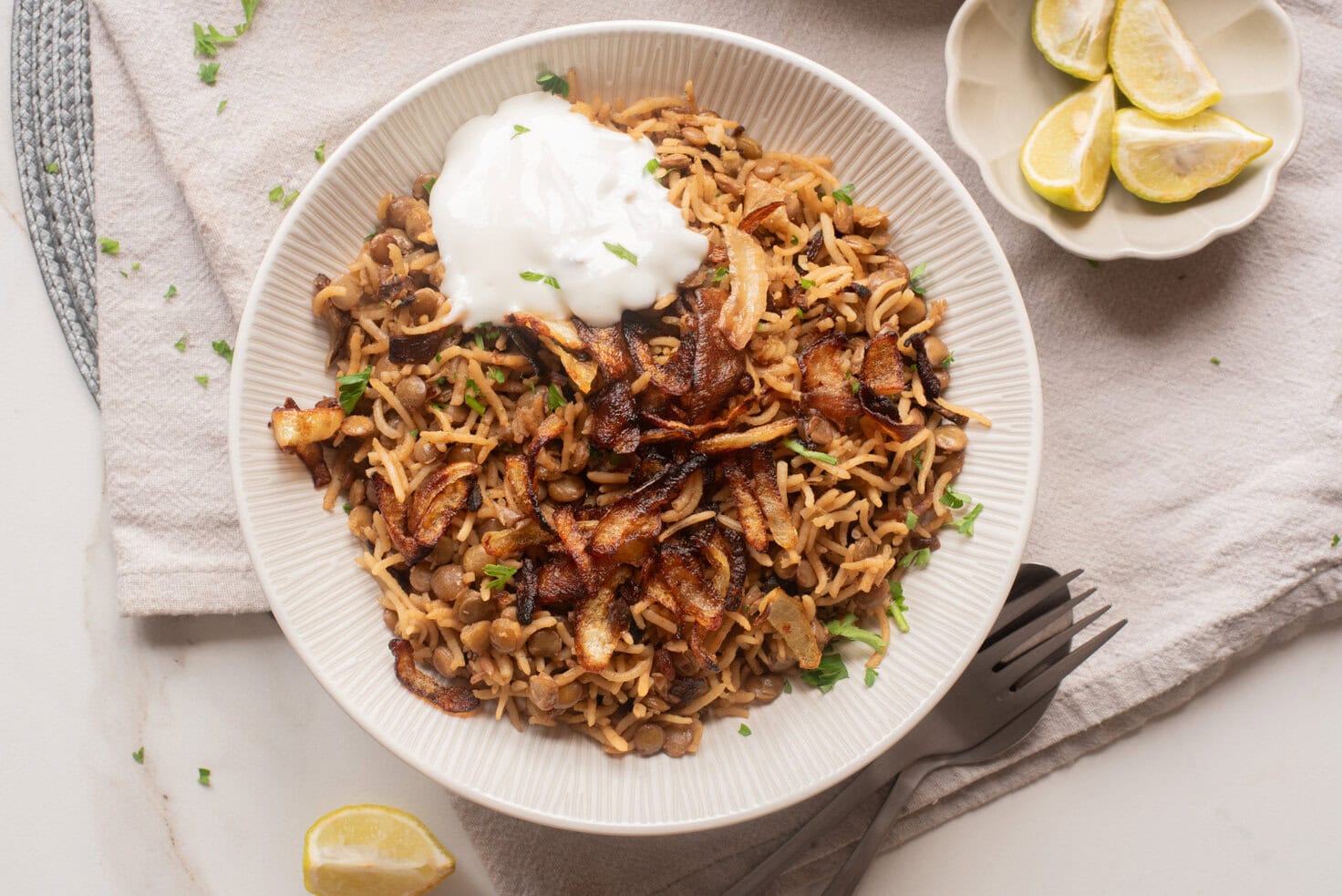 Overhead view of mujaddara served with crispy onions, yogurt, and lemon wedges.