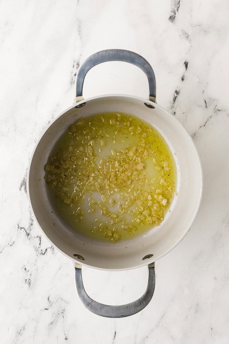 Overhead view of shallot cooking in olive oil in a saucepan.