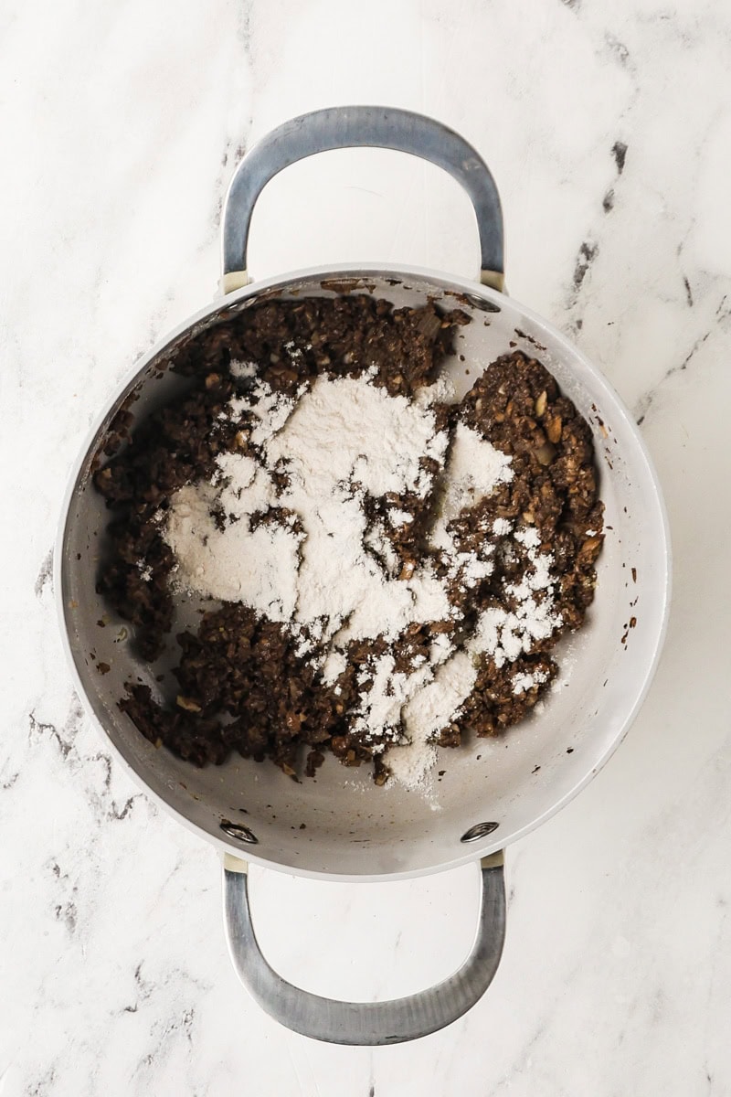 Flour sprinkled over cooked mushrooms in a saucepan.