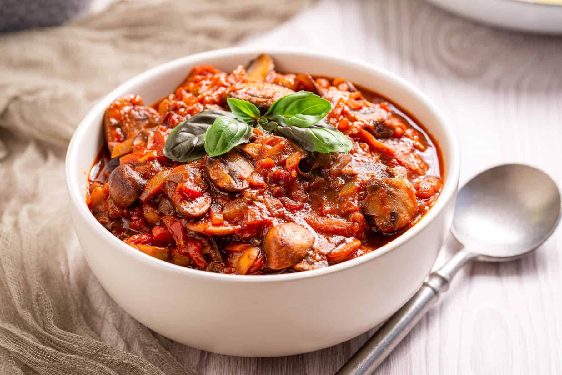 An image of mushroom ragu in a white bowl with a garnish of basil on top.
