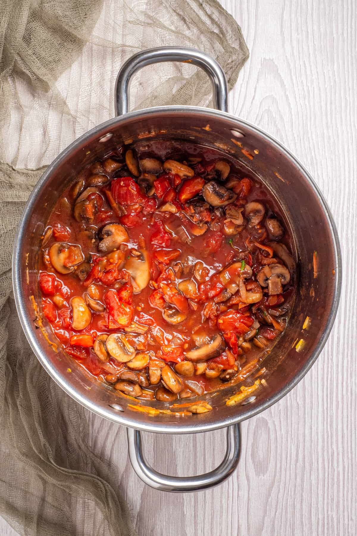 An overhead image of vegan red wine and plum tomatoes being added to the pot of mushroom ragu.