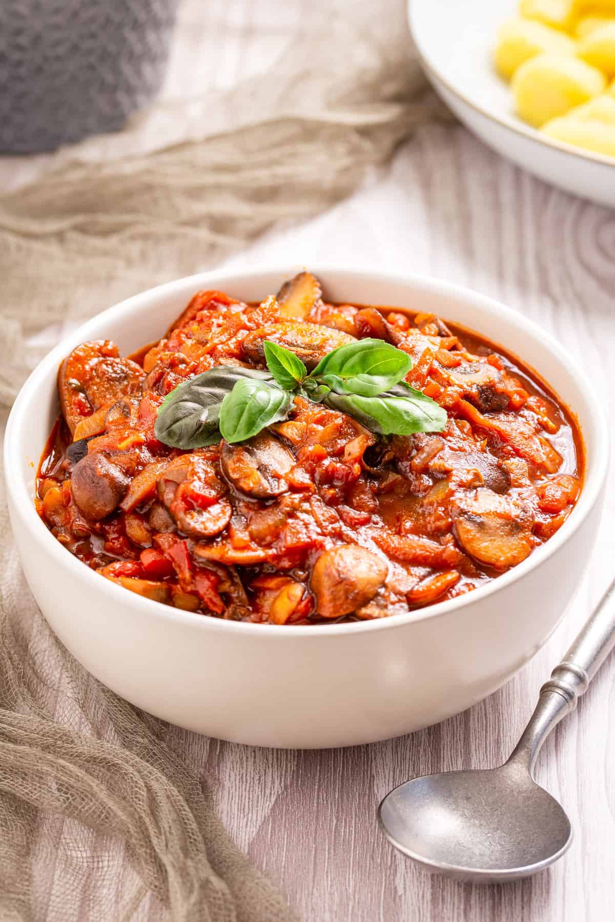 An image of mushroom ragu in a white bowl with a garnish of basil on top.