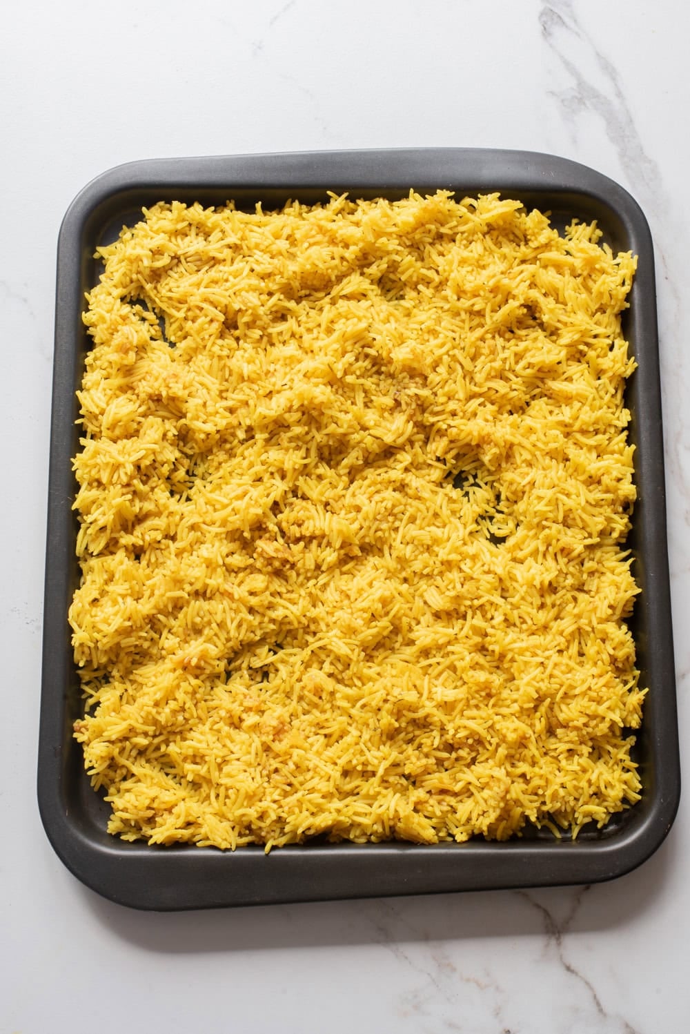Rice spread on a baking tray to cool for fried rice.