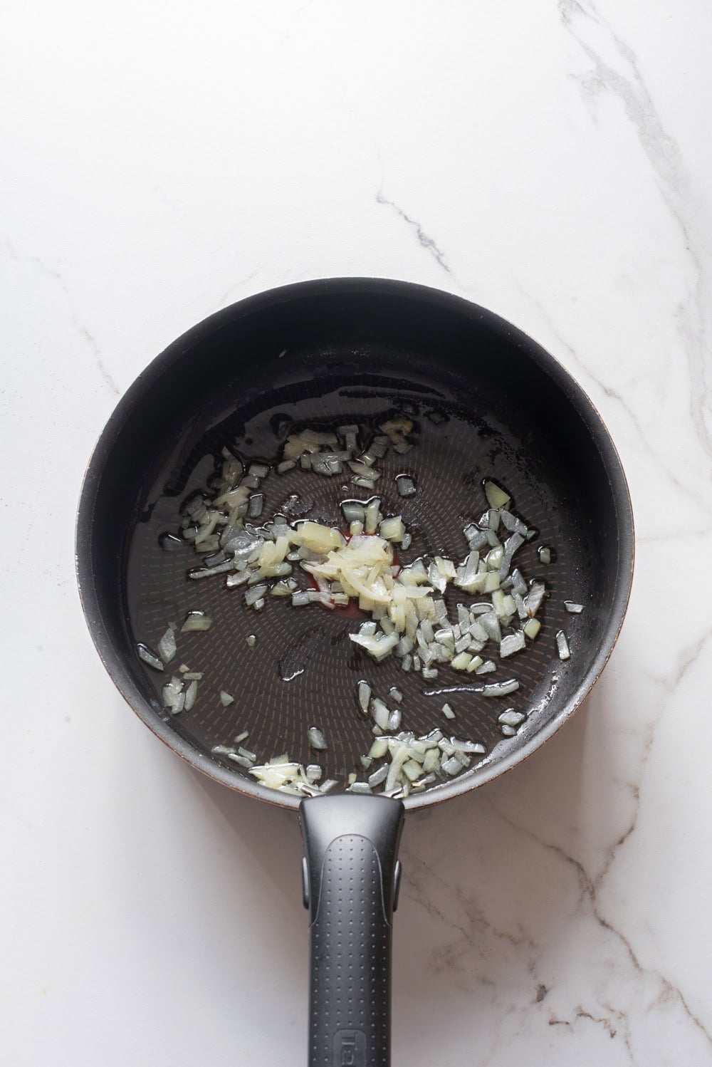Chopped onions sautéing in oil in a pan.
