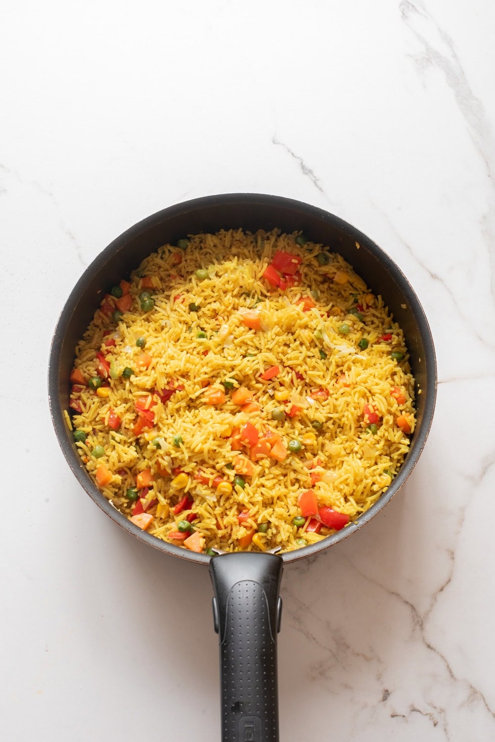 Rice and vegetables tossed together in a pan for Nigerian fried rice.