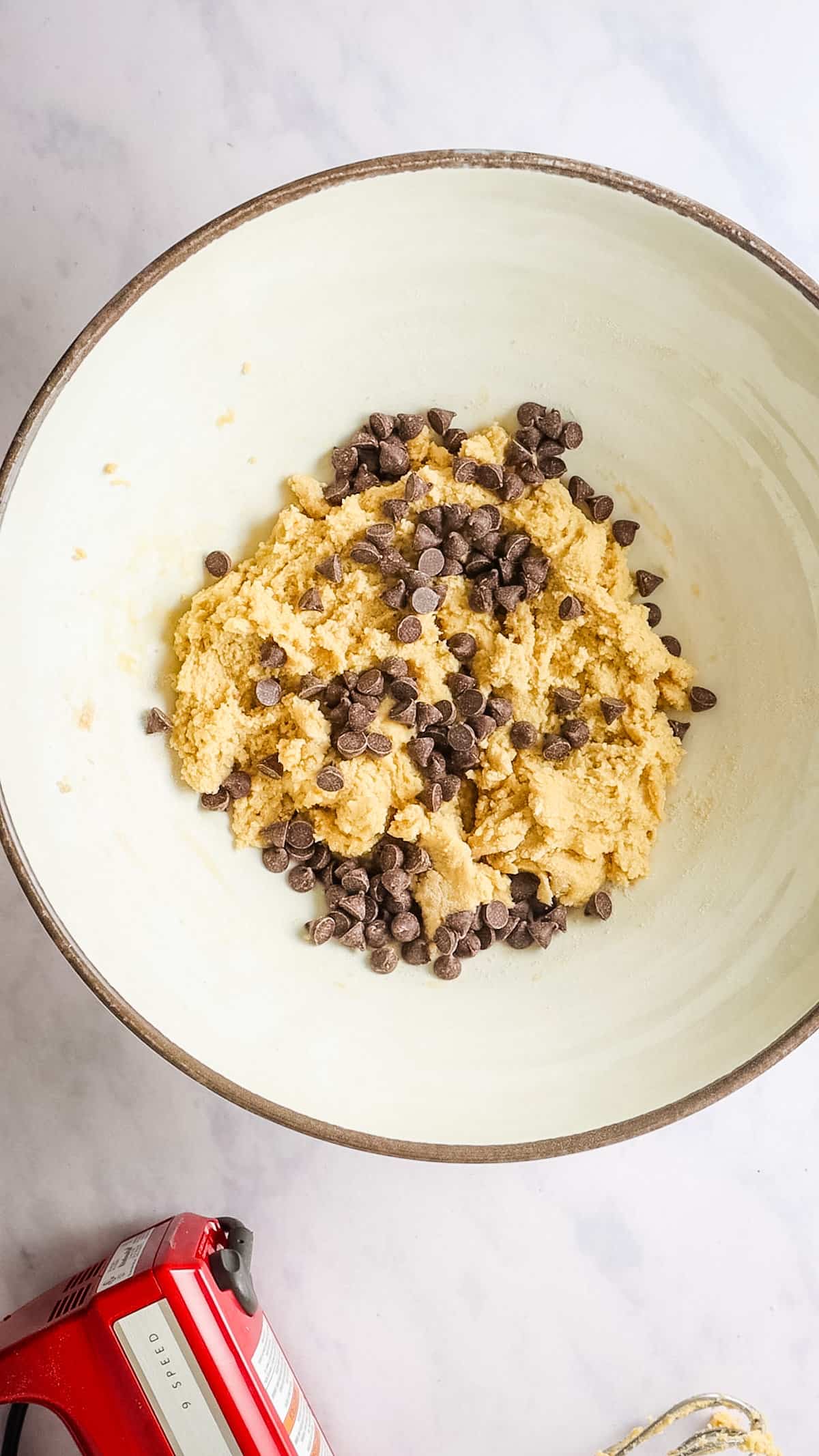 Overhead view of chocolate chips added to mixing bowl with cookie dough.
