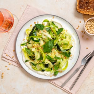 No-cook zucchini ribbon salad with whipped lemon ricotta, basil, mint, toasted pine nuts, and lemon zest served on a white plate.