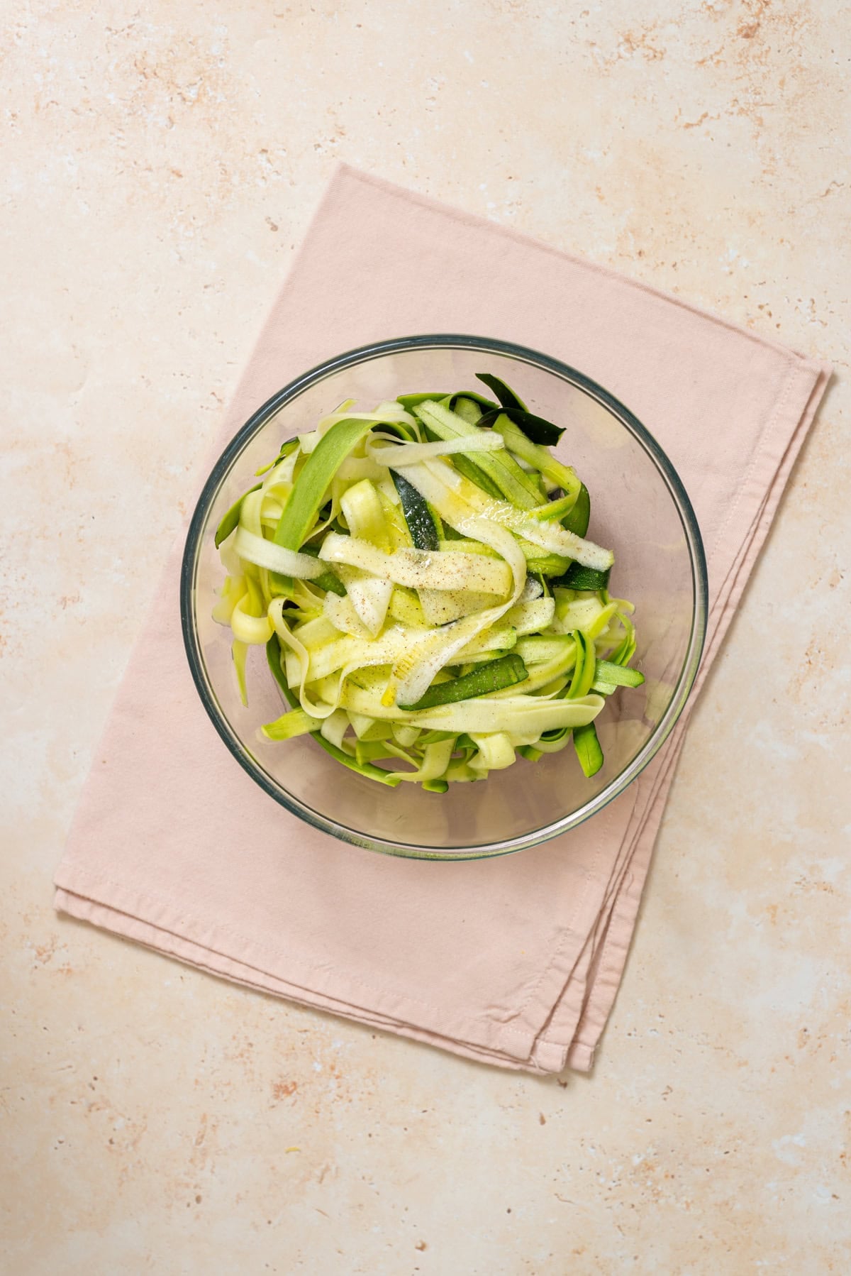 Fresh zucchini ribbons topped with olive oil, lemon juice, and salt in a glass bowl.