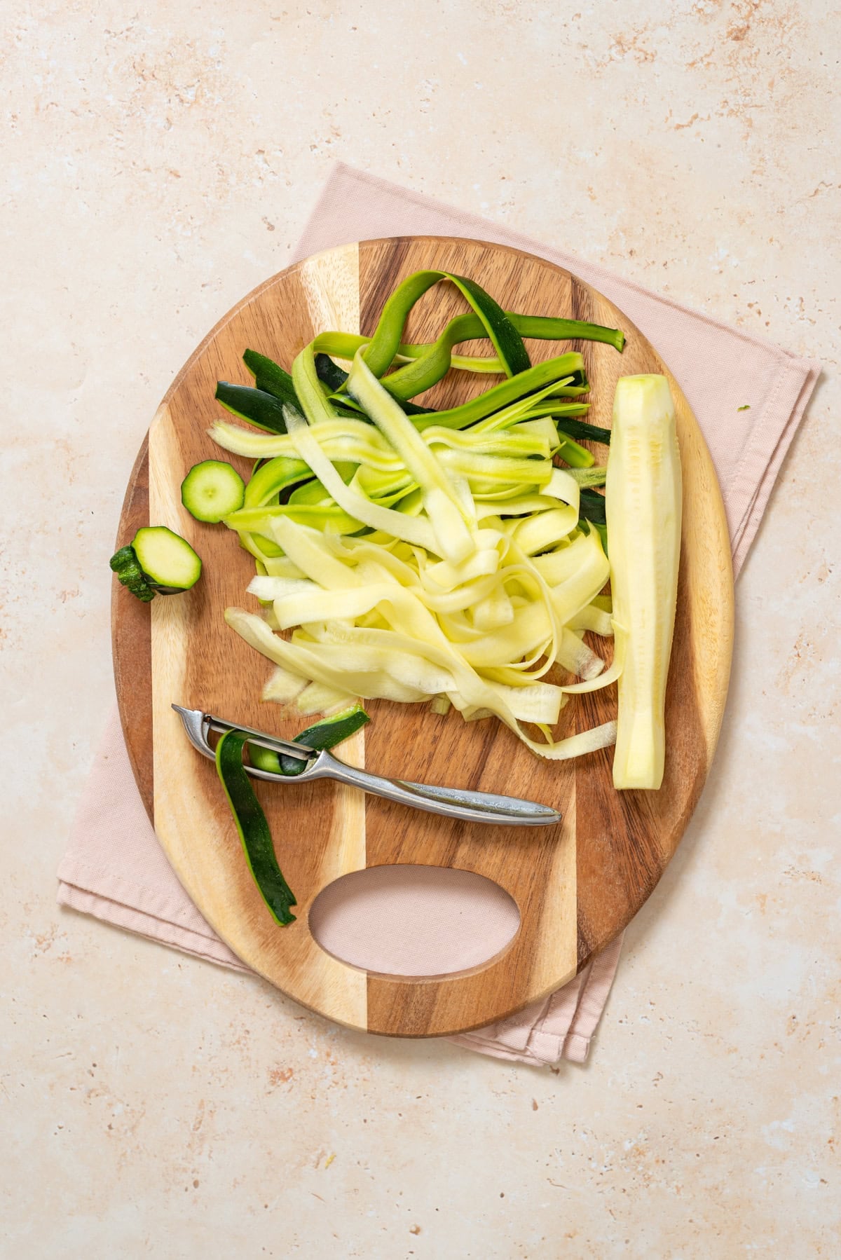 Shaving zucchini into long ribbons with a Y-peeler on a wooden cutting board.