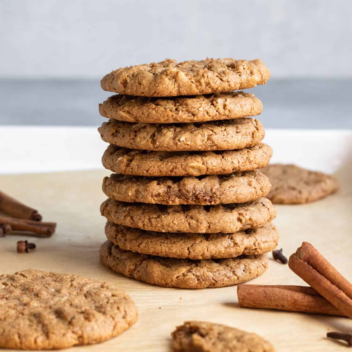 A straight shot of stacked spiced tahini oatmeal cookies with cinnamon sticks on the side.