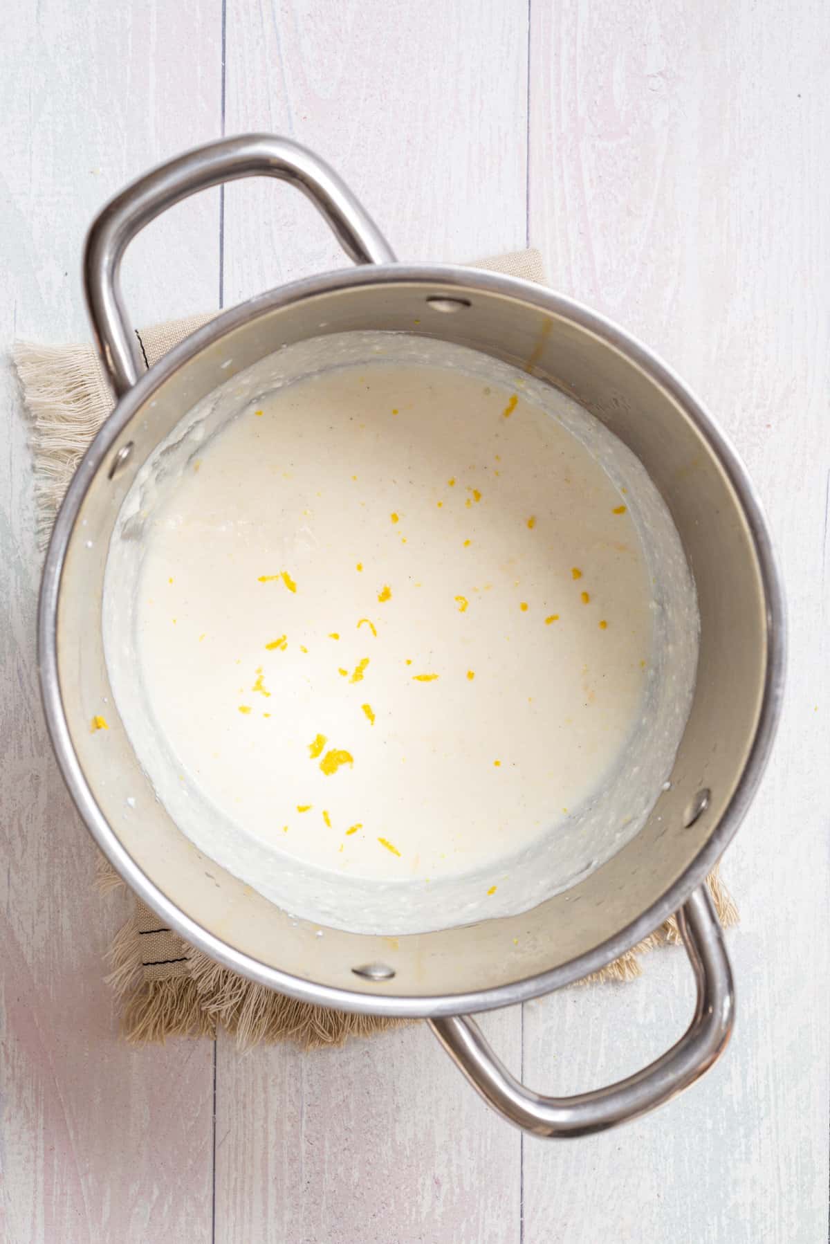 Overhead view of a large pot with mixed ricotta, parmesan, lemon zest, lemon juice, salt, and pepper added to pasta water.