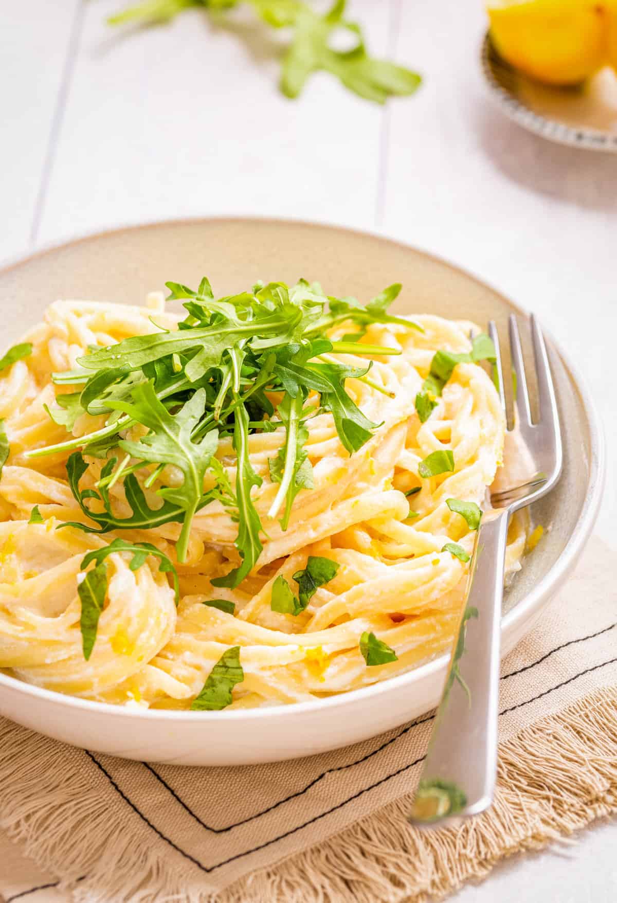 Close-up view of one pot lemon ricotta pasta topped with chopped basil and rocket leaves placed on a plate with a fork on the side.