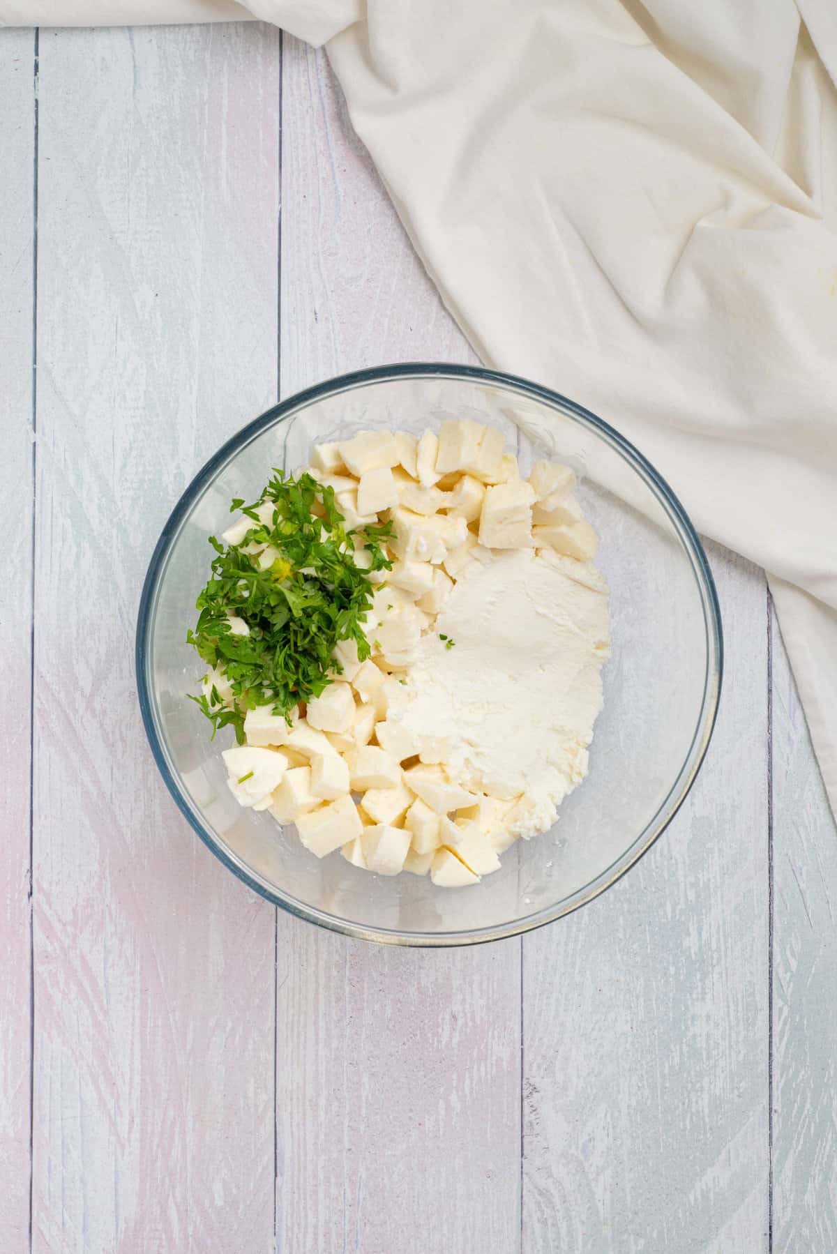 Overhead view of a bowl with unmixed mozzarella cubes, parsley, and ricotta. 