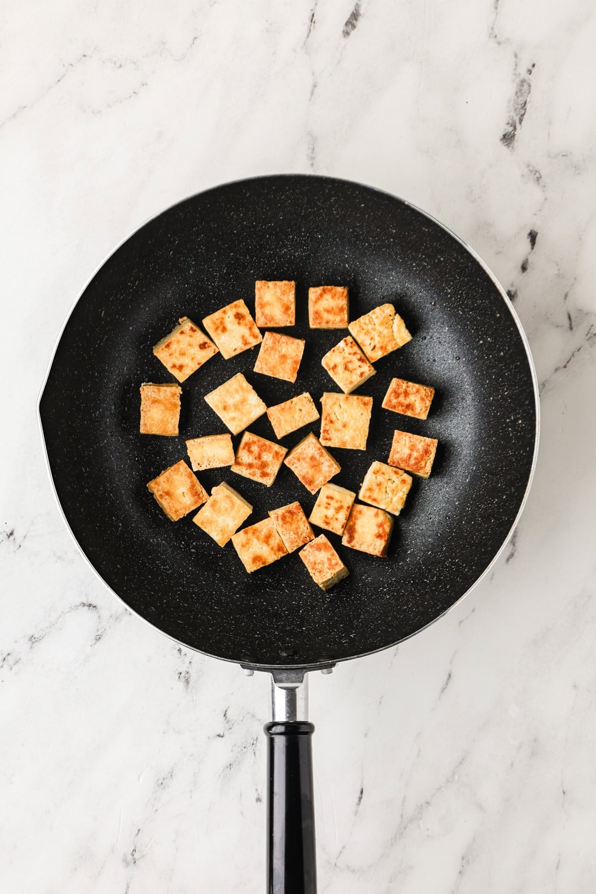An overhead image of searing the tofu in a skillet.
