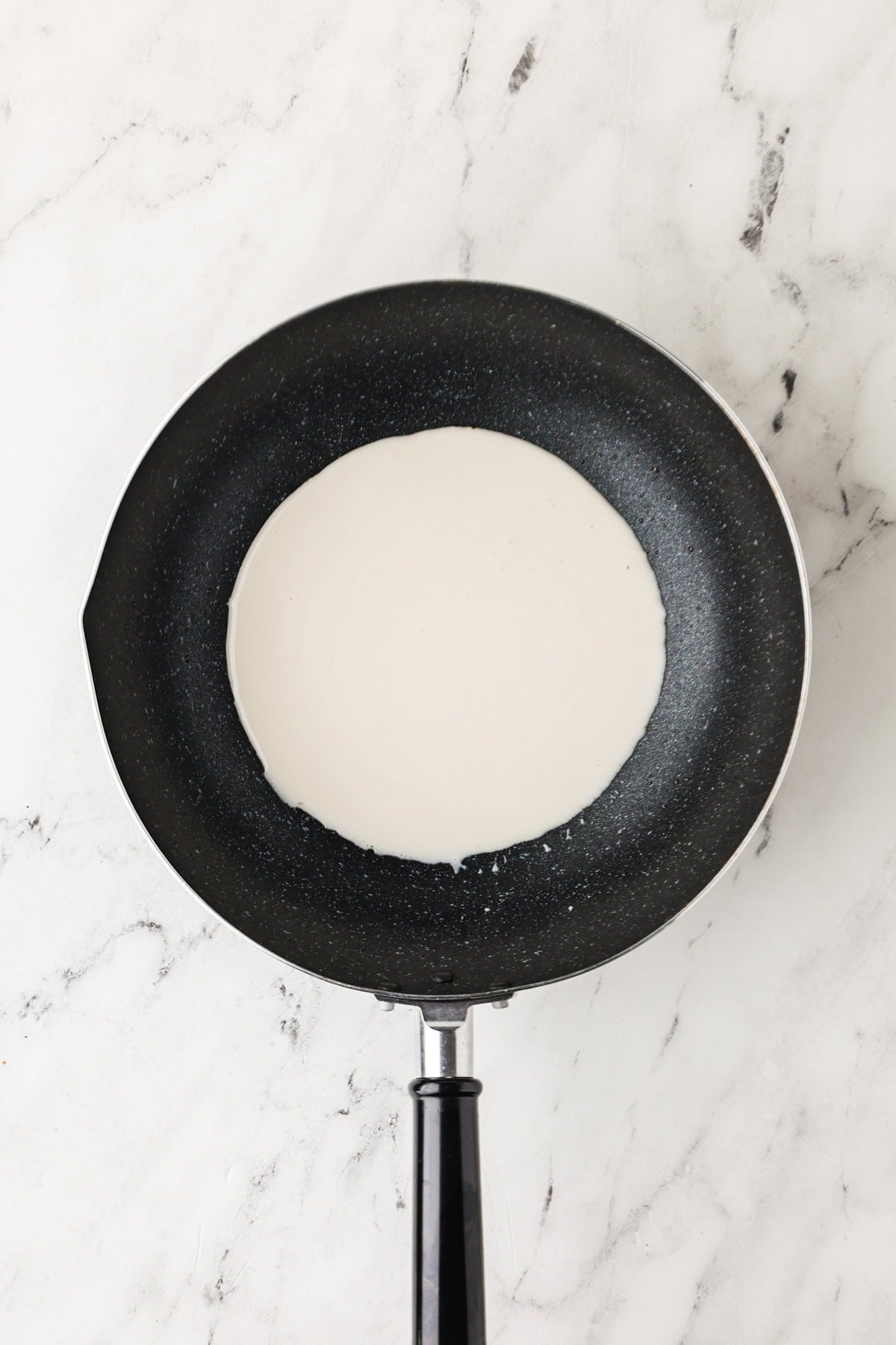 An overhead image of heating the coconut milk in a skillet.