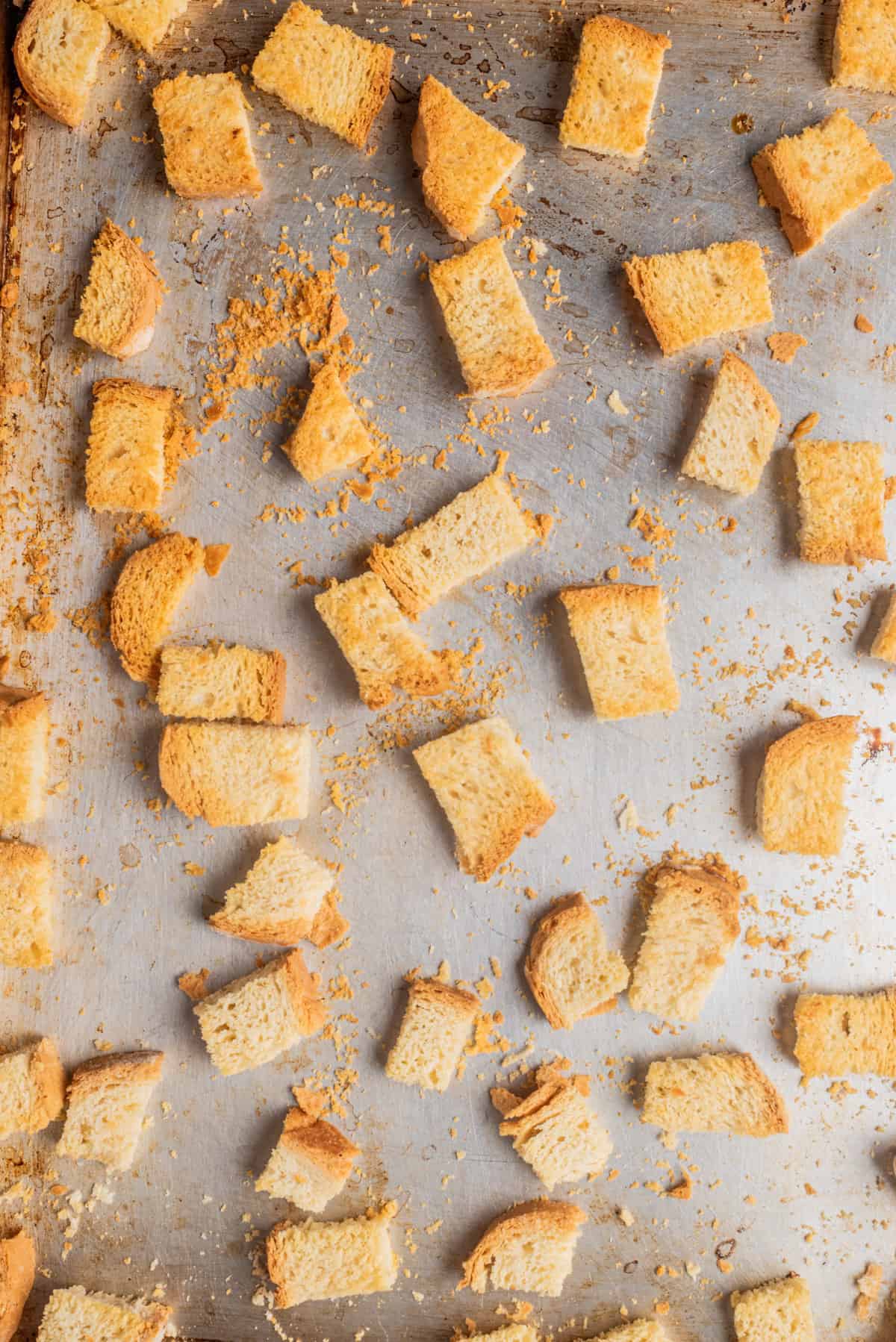 An overhead image of golden brown cubed crusty bread spread out on a baking sheet.