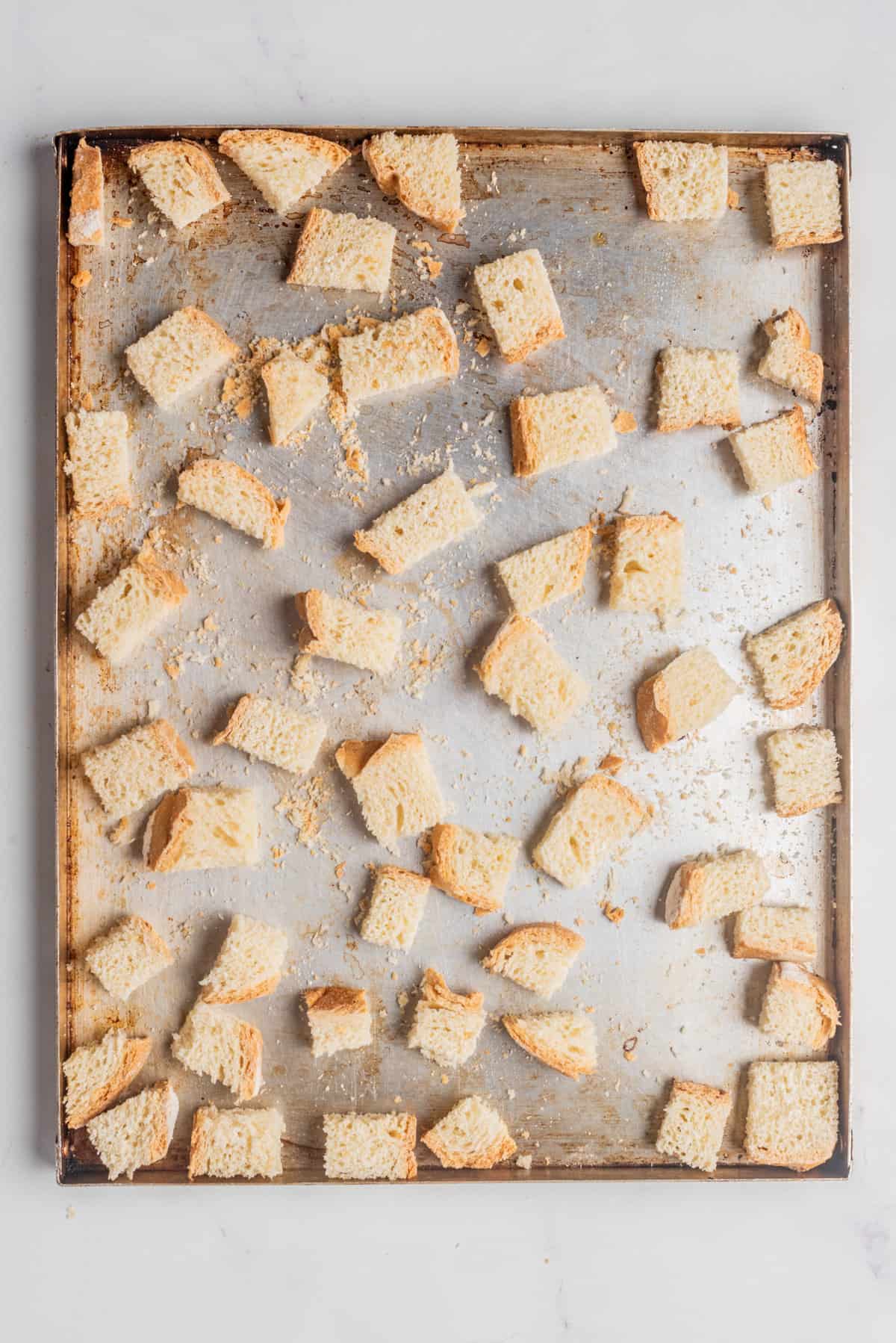 An overhead image of cubed crusty bread spread out on a baking sheet.