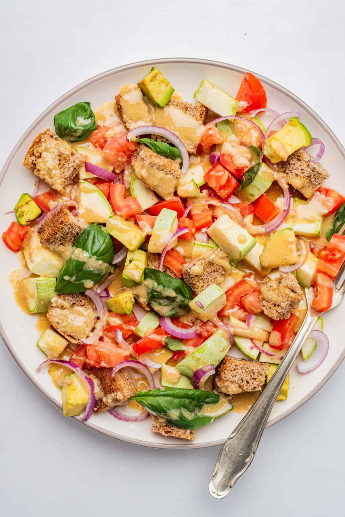 An overhead image of panzanella salad served on a white plate with dressing on top of it.