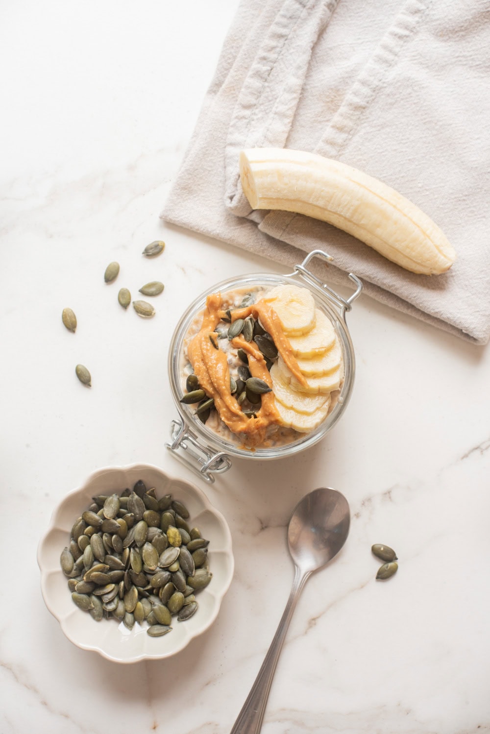 An overhead image of garnishing the oats with bananas, peanut butter, and pepitas.
