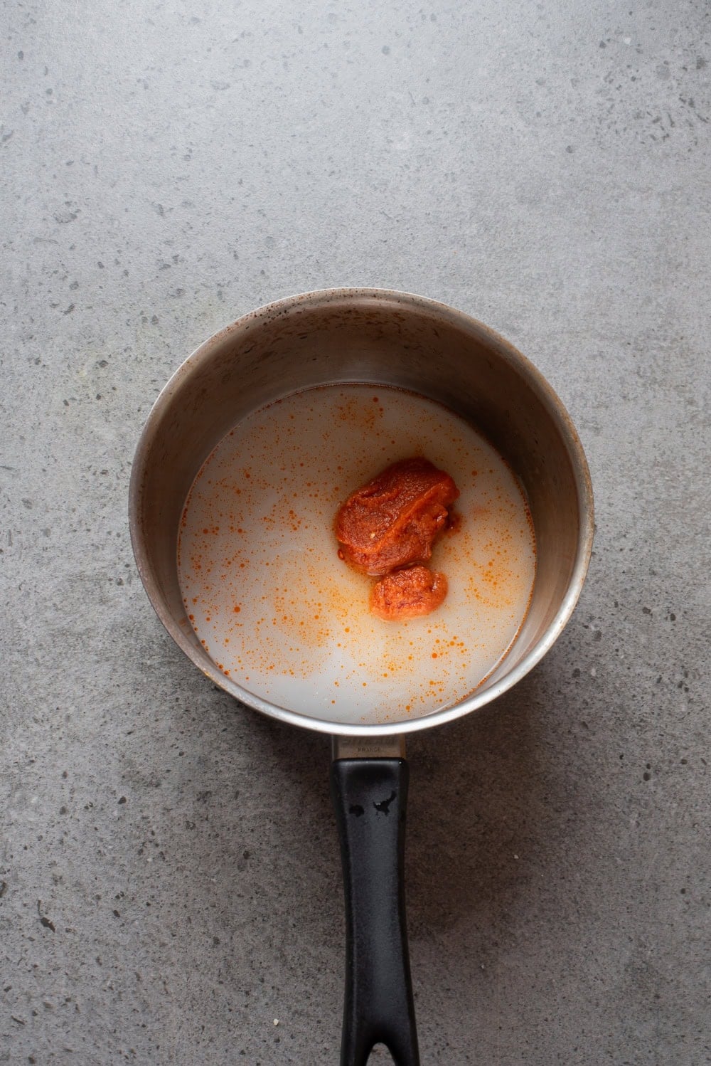 Overhead image of red curry paste added to coconut milk in a pan.