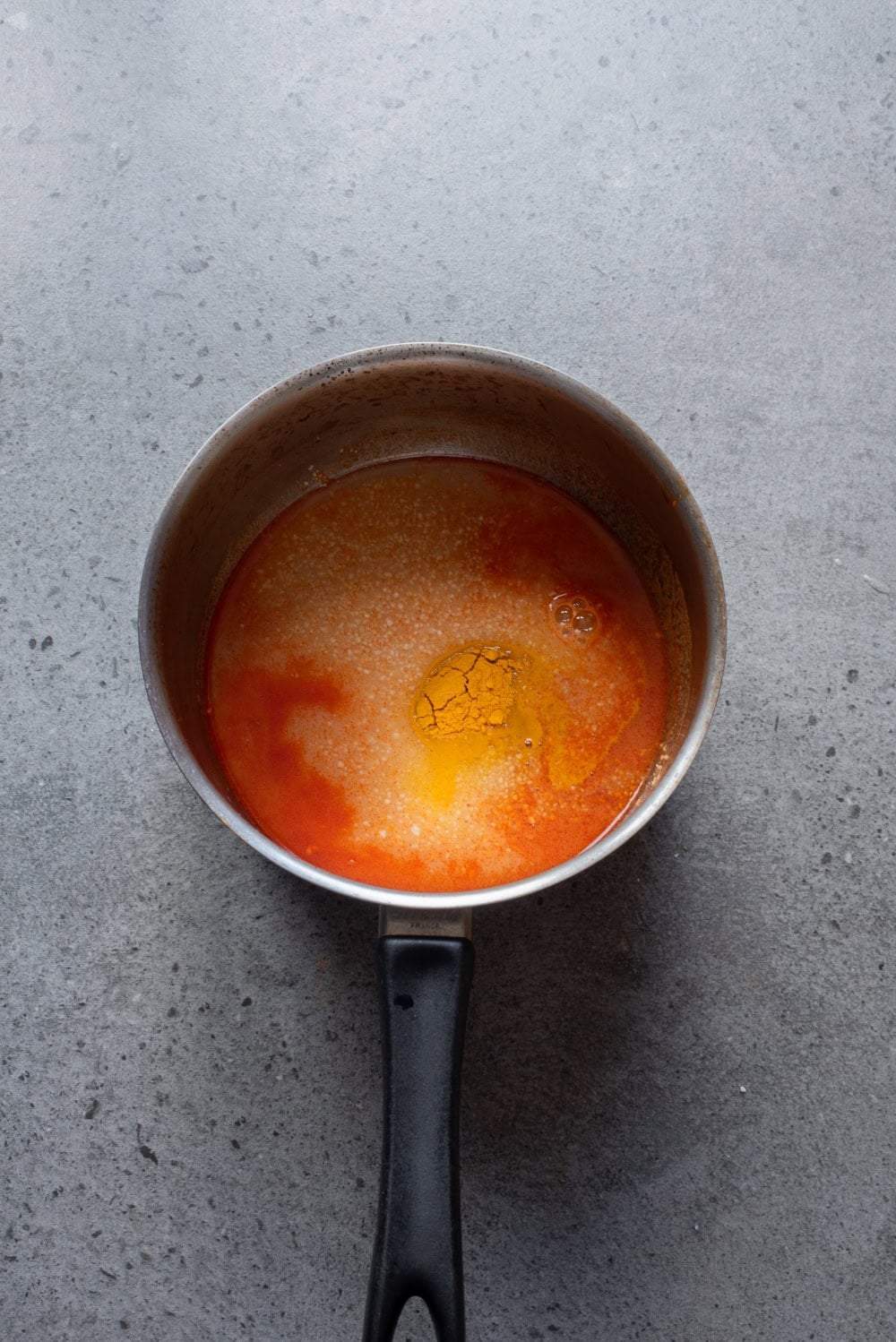 Overhead image of the remaining ingredients of peanut sauce added in the bloomed red curry paste in a pan.